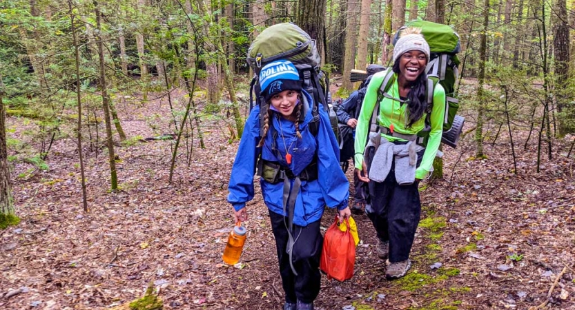 two girls smile as they backpack on an outward bound course